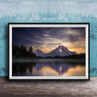 The image is a framed photograph of a serene mountain landscape at sunset, with a calm lake reflecting the vibrant colors of the sky.