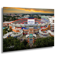 a large stadium with a large sign that reads "UF Florida", surrounded by a cityscape and a colorful sunset sky.