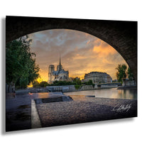 a serene cityscape with a large cathedral in the background, set against a vibrant orange and blue sky at sunset. The cathedral is framed by a stone archway, adding a sense of grandeur to the scene. The photograph is taken from a low angle, emphasizing the height of the cathedral and the archway. The overall composition is visually striking and evokes a sense of tranquility and beauty.