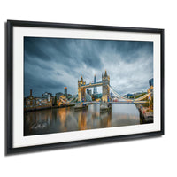 A framed photograph of the Tower Bridge in London, England, with the bridge illuminated against a cloudy sky.