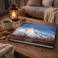 a wooden coffee table with a book titled "Clifton Haley Photography" on it, along with a lit candle, a mug of coffee, and some fallen leaves.