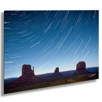 A stunning night landscape featuring three iconic rock formations silhouetted against a starry sky, with a trail of light streaking across the sky.