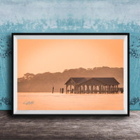 A framed photograph of a wooden pier extending into a body of water, with a warm orange and yellow sunset sky in the background.