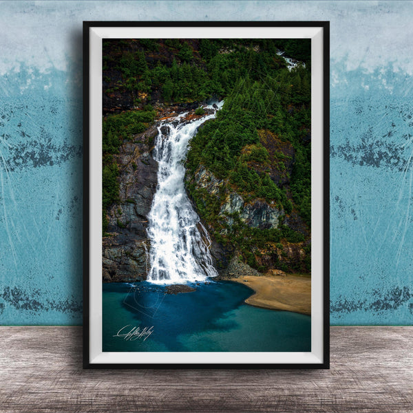 A framed photograph of a waterfall cascading down a rocky cliff surrounded by lush greenery, with a blue-green body of water below.