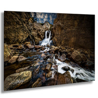 A serene waterfall cascades over rocks in a rocky canyon, surrounded by lush greenery and a cloudy sky.