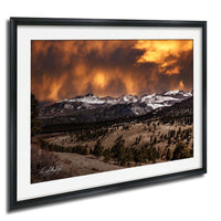 a breathtaking mountain landscape with snow-capped peaks, a dramatic orange and yellow sky, and a forested valley below.