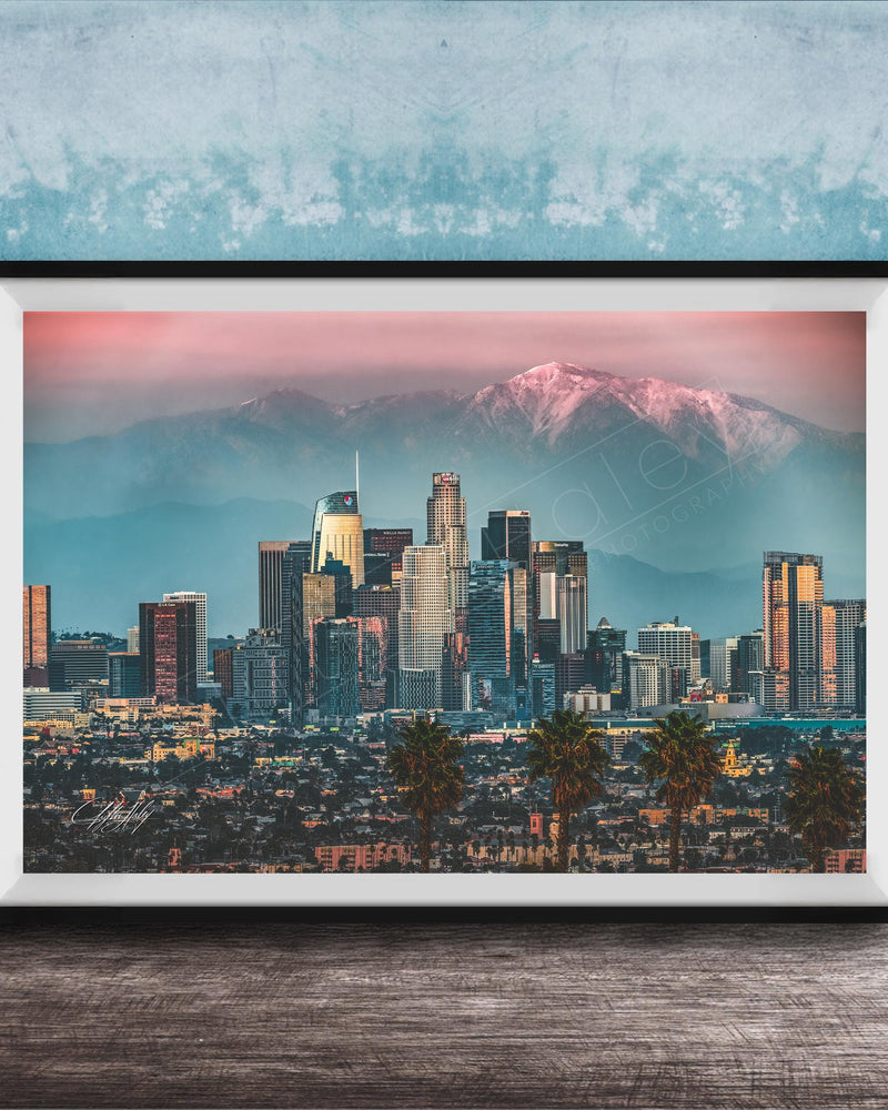 A framed photograph of the Los Angeles skyline at sunset, with the city's skyscrapers and mountains in the background.