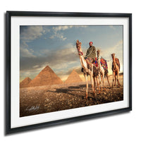 A man rides a camel in front of the iconic pyramids of Giza, Egypt, with the sun setting in the background.