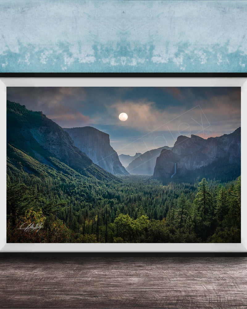 The image is a framed photograph of a mountainous landscape with a full moon in the sky, surrounded by trees and forests.