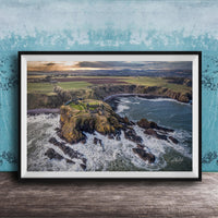 The image is a framed aerial view of a coastal landscape, featuring a rocky outcrop, a small island, and the ocean.