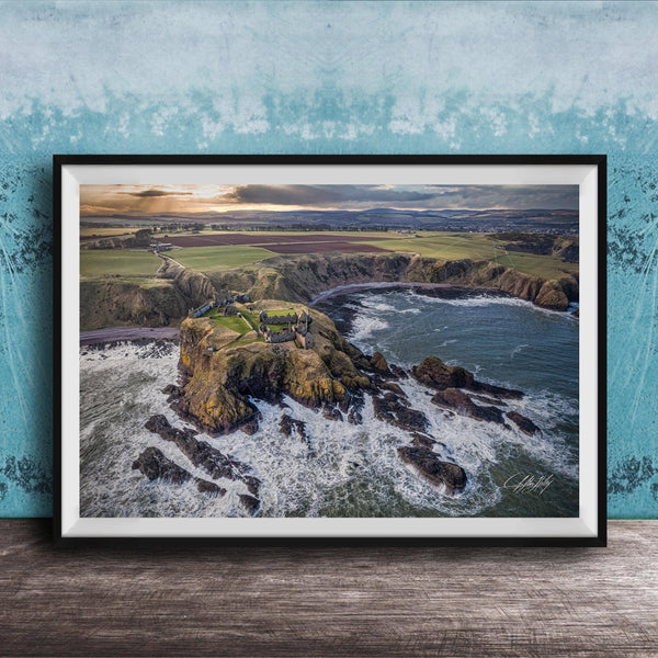 The image is a framed aerial view of a coastal landscape, featuring a rocky outcrop, a small island, and the ocean.