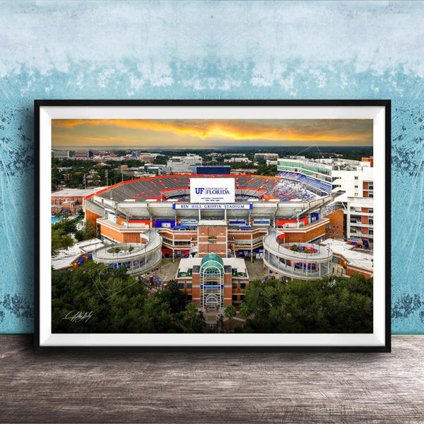 The image is a framed photograph of the Ben Hill Griffin Stadium inUF, Florida, with a sunset sky in the background.