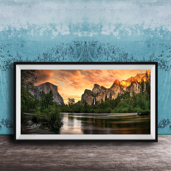 A framed photograph of a scenic mountain landscape at sunset, with a river flowing through the foreground and a waterfall cascading down the mountainside.
