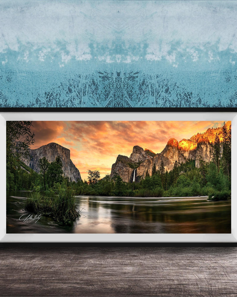 A framed photograph of a scenic mountain landscape at sunset, with a river flowing through the foreground and a waterfall cascading down the mountainside.