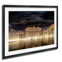 A framed photograph depicting the Bellagio Fountains in Las Vegas at night, with the fountains illuminated and creating a stunning reflection on the water surface.