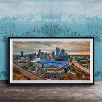 The image is a framed aerial view of a city skyline, featuring a large stadium with a distinctive blue roof.