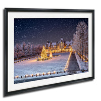 A large, illuminated building with a Christmas tree in the foreground, surrounded by snow-covered trees and a snowy landscape.