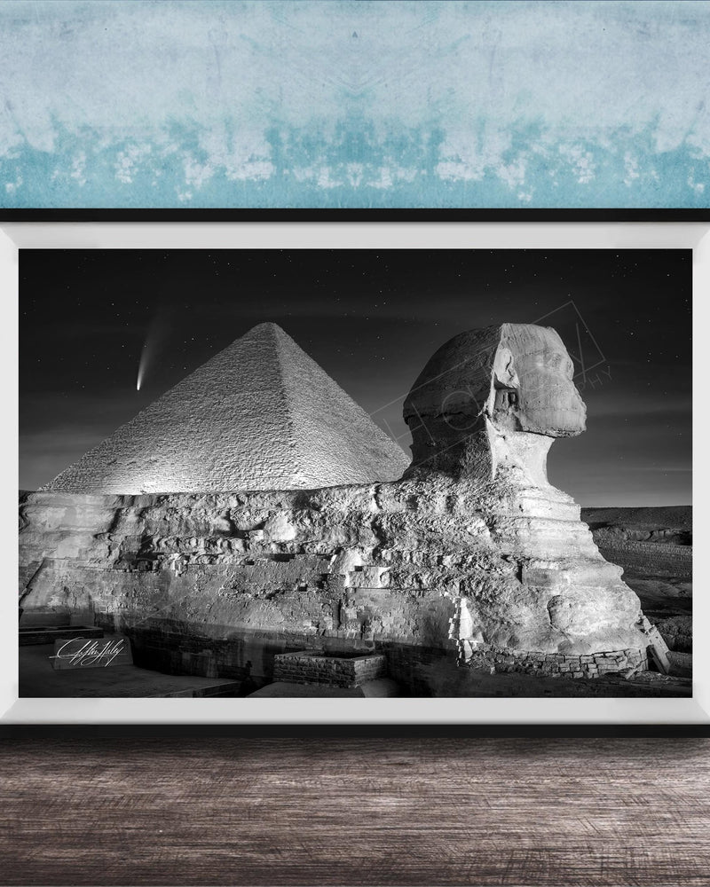 A black and white photograph of the Great Sphinx and the Pyramid of Giza against a night sky, with a small shooting star visible in the sky.