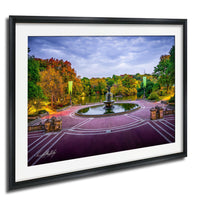 A framed photograph depicting a serene park scene with a fountain, trees, and a lake, all bathed in the warm glow of a colorful autumn sky.