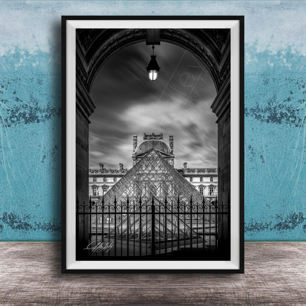 A framed black and white photograph of the Louvre Museum in Paris, France, with the iconic glass pyramid structure of the museum prominently featured.