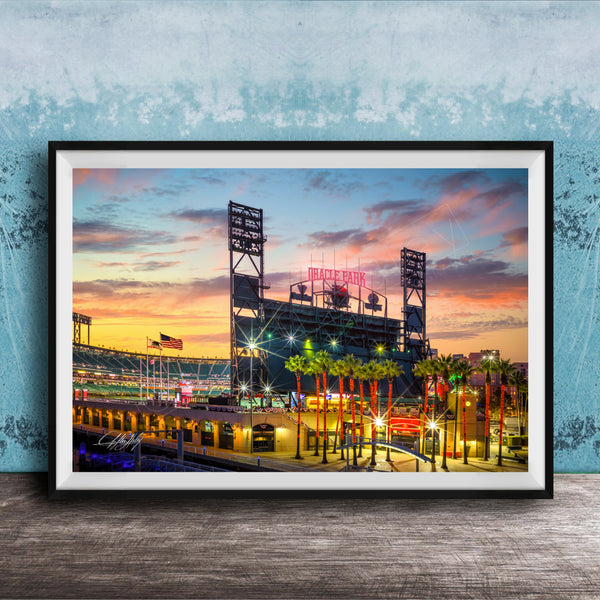 A framed photograph of a baseball stadium at sunset, with the stadium's lights and surrounding palm trees illuminated against a colorful sky.