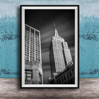 A black and white photograph of the Empire State Building, a famous skyscraper in New York City, with a blue wall in the background.