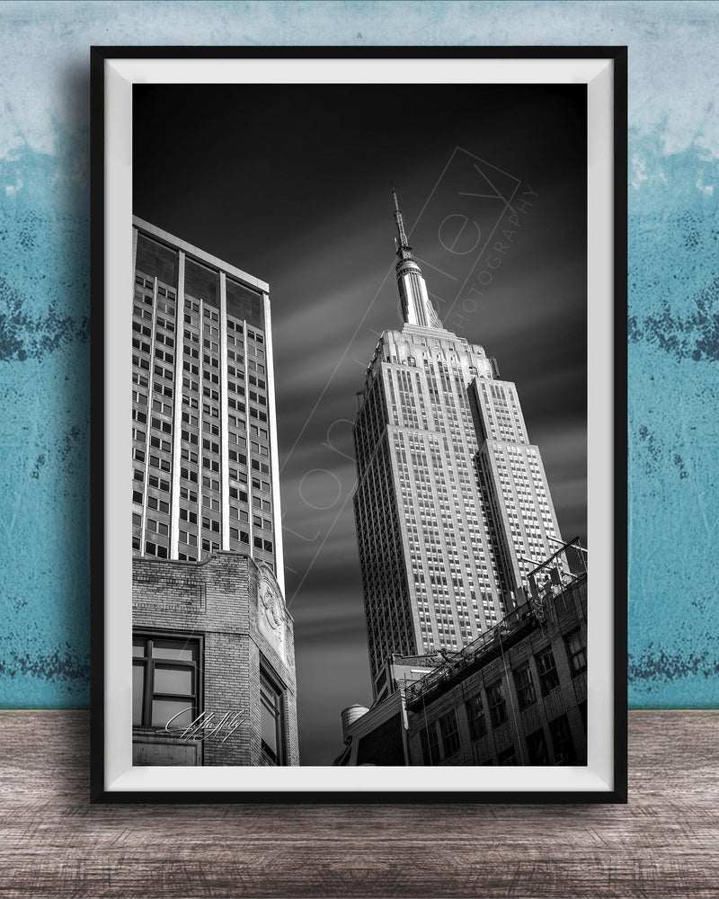 A black and white photograph of the Empire State Building, a famous skyscraper in New York City, with a blue wall in the background.
