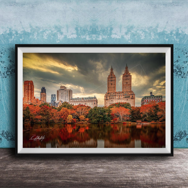 a cityscape with tall buildings and a lake in the foreground, surrounded by trees with autumn foliage.