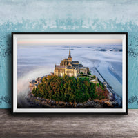 A framed photograph of the iconic Mont Saint-Michel island in Normandy, France, with its distinctive castle perched on a rocky outcrop surrounded by lush greenery.