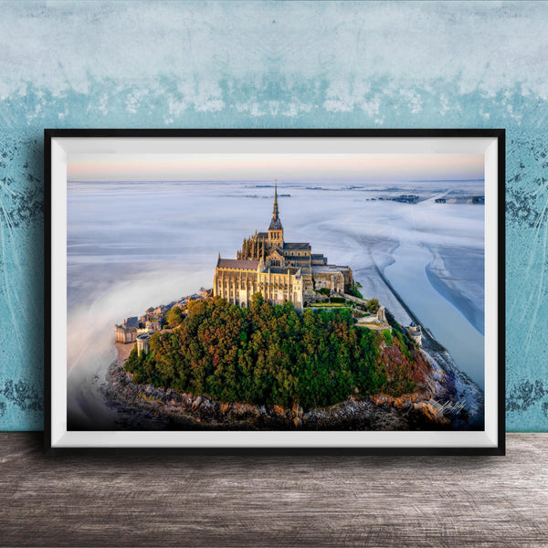 A framed photograph of the iconic Mont Saint-Michel island in Normandy, France, with its distinctive castle perched on a rocky outcrop surrounded by lush greenery.