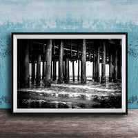 A black and white photograph of a pier with multiple columns and pillars, set against a blue textured wall.