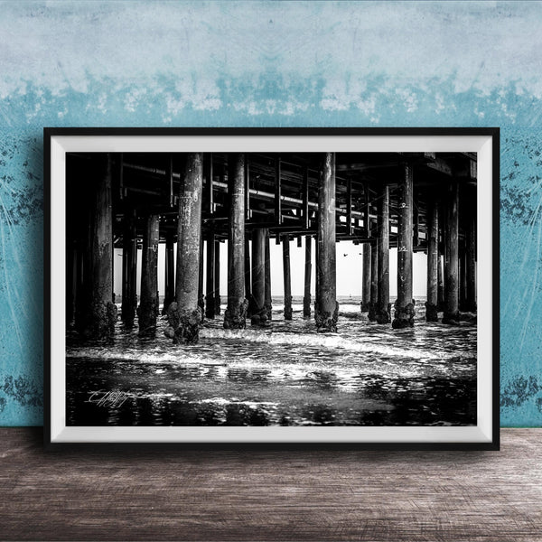 A black and white photograph of a pier with multiple columns and pillars, set against a blue textured wall.