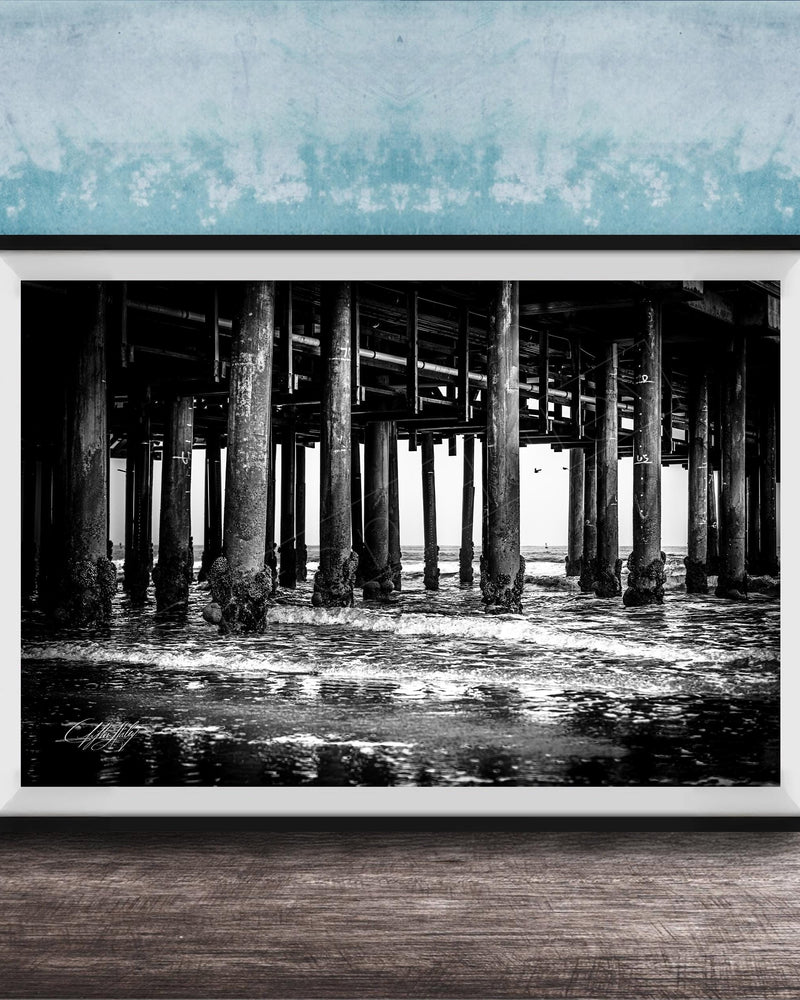 A black and white photograph of a pier with multiple columns and pillars, set against a blue textured wall.