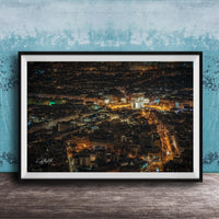 The image is a framed aerial view of a city at night, showcasing the illuminated buildings and streets below.