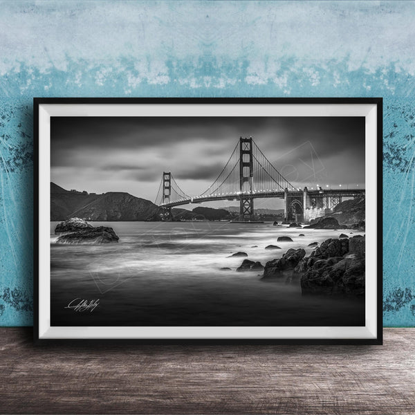 A black and white photograph of the Golden Gate Bridge in San Francisco, California, with the bridge's towers and suspension cables prominently featured against a cloudy sky.