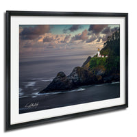 A framed photograph depicting a lighthouse on a rocky cliff overlooking the ocean at sunset.