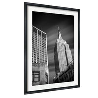 A black and white photograph of the Empire State Building, a famous skyscraper in New York City, captured in a framed black frame.