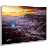 a breathtaking view of the Grand Canyon, with a winding river flowing through the rugged, layered rock formations. The sky is painted in warm hues of orange and yellow, creating a stunning backdrop for the natural landscape. The image is a captivating representation of the Grand Canyon's beauty and grandeur.