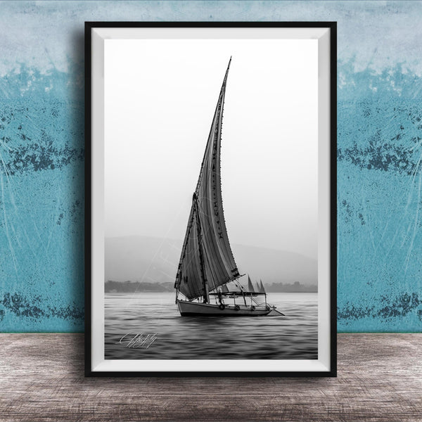 This luxury black and white fine art photograph captures a felucca sail boat drifting along the Nile River at sunset near Luxor, Egypt. Soft fog and minimalist composition create a timeless, monochrome aesthetic rooted in Egyptian river culture. Ideal for collectors and interior designers seeking refined, museum-quality wall art that embodies elegance, simplicity, and enduring calm.