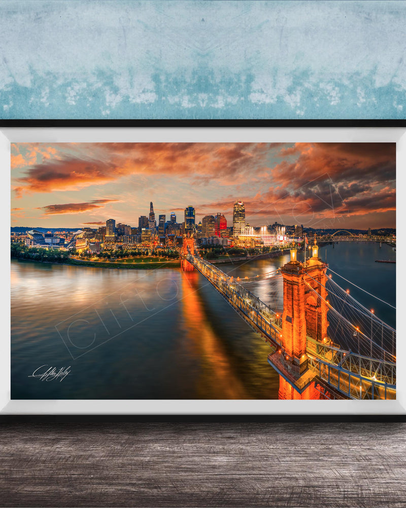 A framed photograph of the Cincinnati skyline at sunset, with the city's iconic landmarks and bridges illuminated against a dramatic sky.