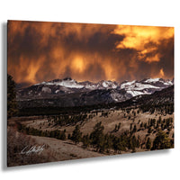 a breathtaking mountain landscape with snow-capped peaks, a dramatic orange and yellow sky, and a lush green forest in the foreground.