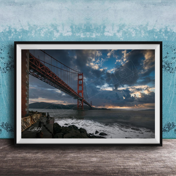 A framed photograph of the Golden Gate Bridge in San Francisco, California, with dramatic clouds and a sunset sky in the background.
