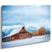 A rustic wooden barn stands in a snowy landscape, with snow-capped mountains in the background and a cloudy sky above.