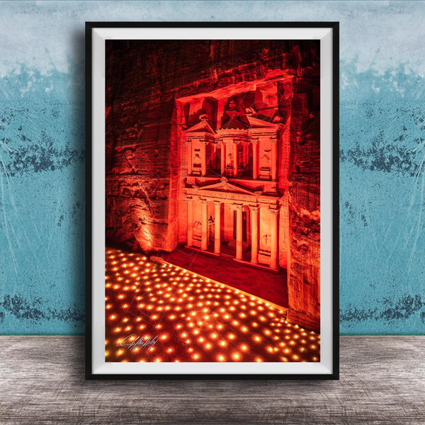 The image is a framed photograph of a large, illuminated structure, possibly a temple or monument, with a red and orange glow illuminating the scene. The photograph is set against a blue wall, creating a striking contrast between the illuminated structure and the surrounding environment.