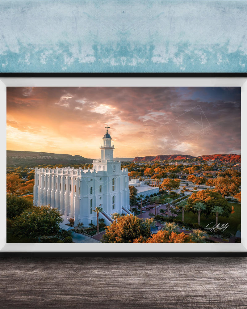 A framed photograph of a white temple with a tower, set against a colorful sunset sky with clouds and mountains in the background.