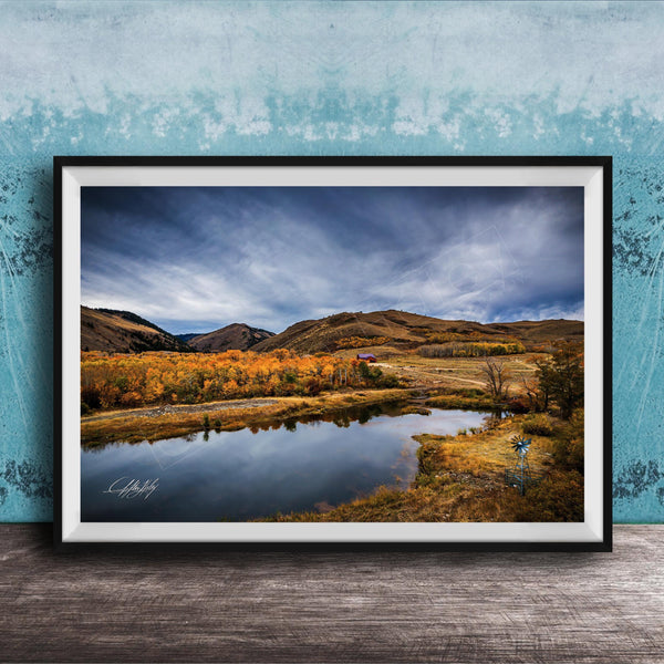The image is a framed photograph depicting a serene landscape with a lake, mountains, and trees in autumn colors.