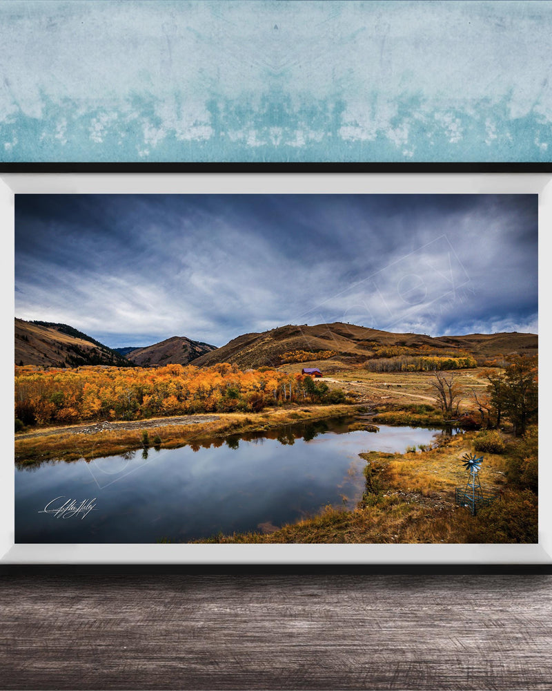 The image is a framed photograph depicting a serene landscape with a lake, mountains, and trees in autumn colors.