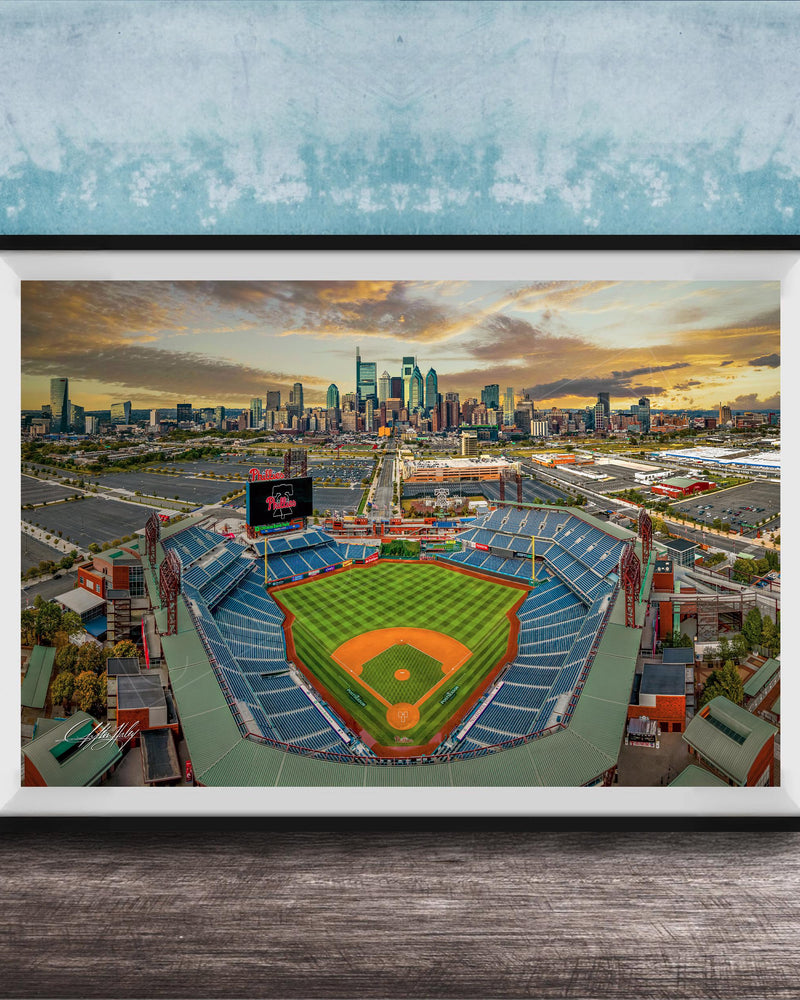 The image is a framed photograph of a baseball stadium in a city, with the city skyline visible in the background.