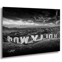 The image is a black and white photograph of the Hollywood Sign, a famous landmark in Los Angeles, California. The sign is prominently displayed in the foreground, with the city skyline visible in the background. The sky above the sign is filled with clouds, creating a dramatic and moody atmosphere. The image is a striking and visually appealing composition, capturing the iconic Hollywood Sign and the surrounding landscape.