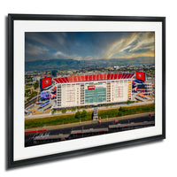 a large stadium with a red roof and various advertisements, surrounded by a cityscape and mountains in the background.